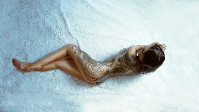 svlečená tetovaná žena na posteli 